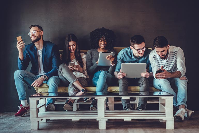 Diverse group of people sittin on a sofa and using their device of preference