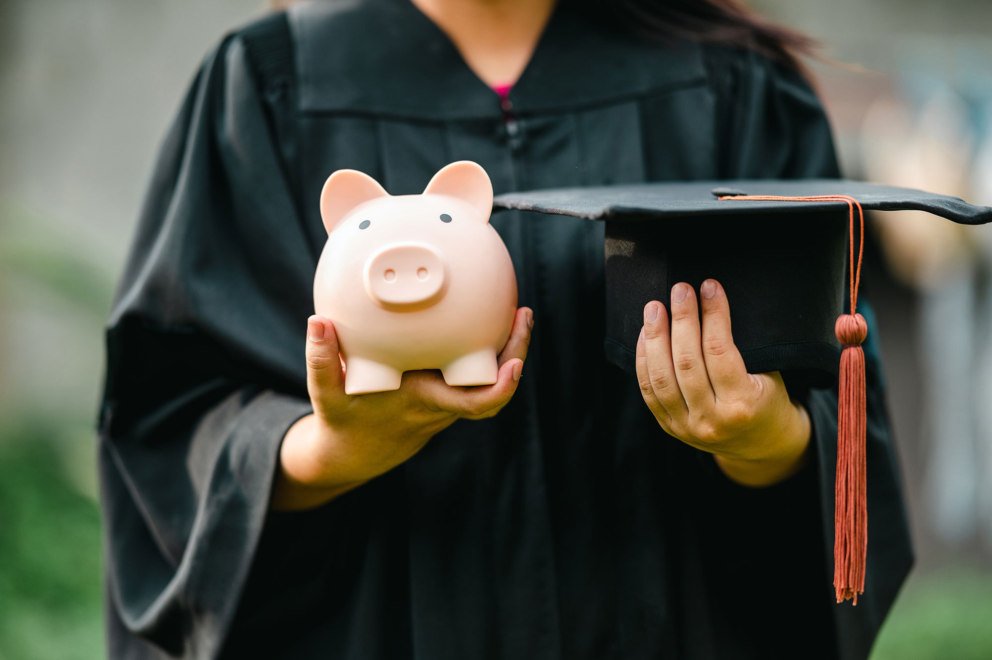 Balancing education and savings. Student a Piggy Bank and a Graduation Cap on each hand.